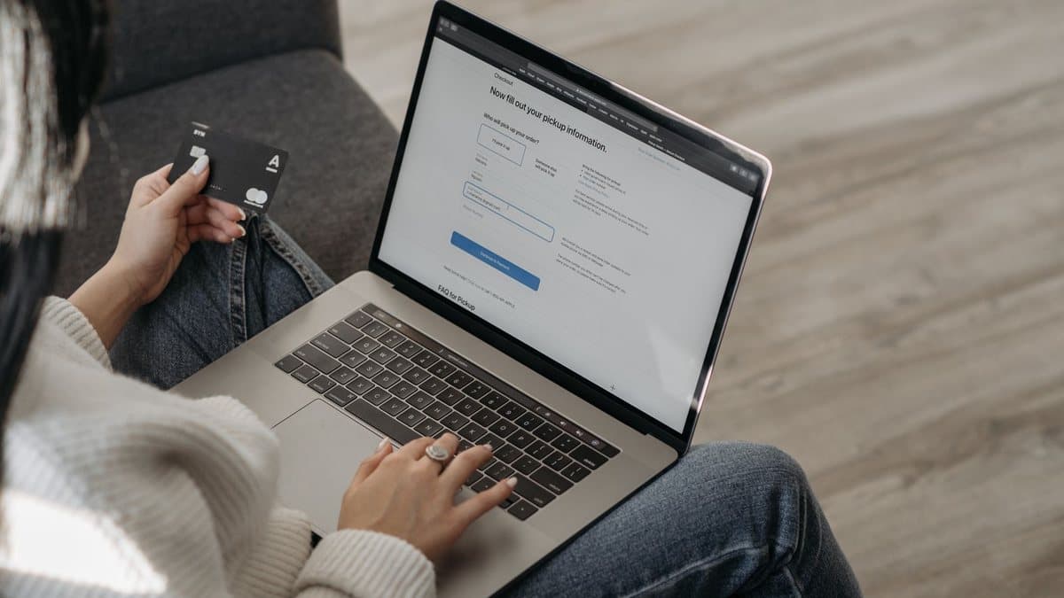 Person holding a card while browsing a laptop, considering a trial subscription