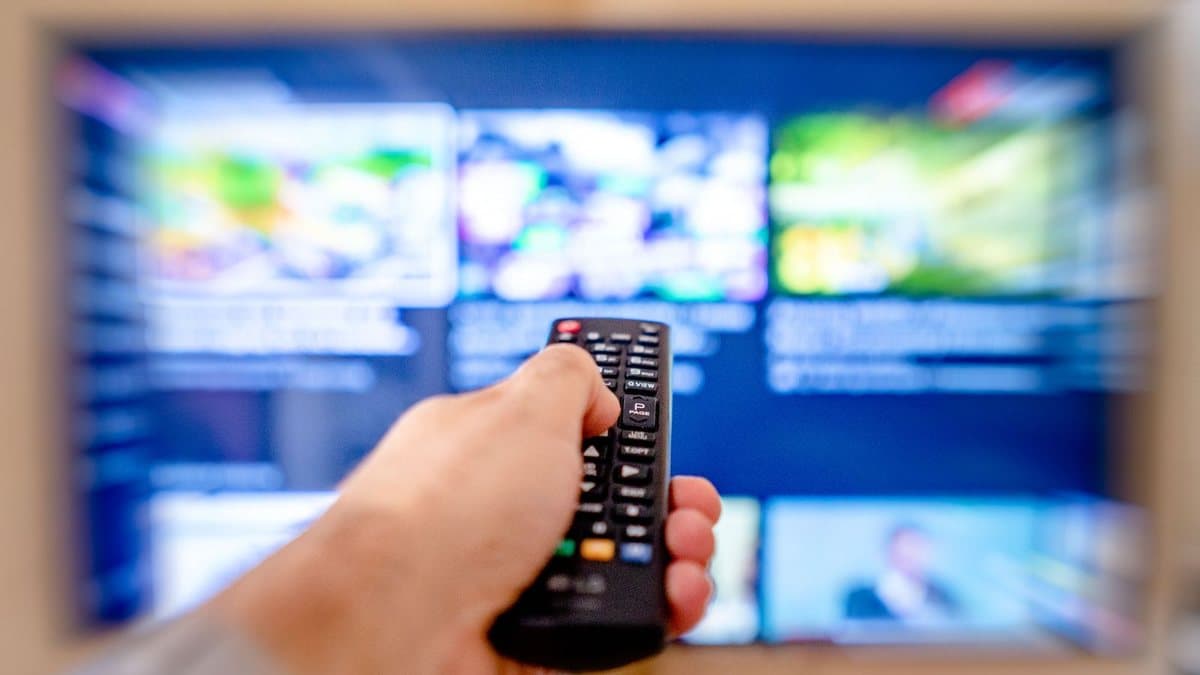 Close-up of a hand using a streaming remote control in front of a television