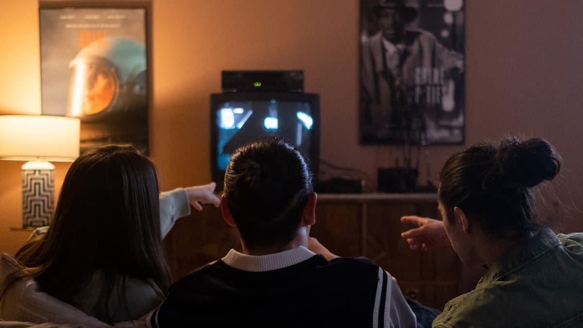Friends sitting together on a couch, pointing at the television while watching a match