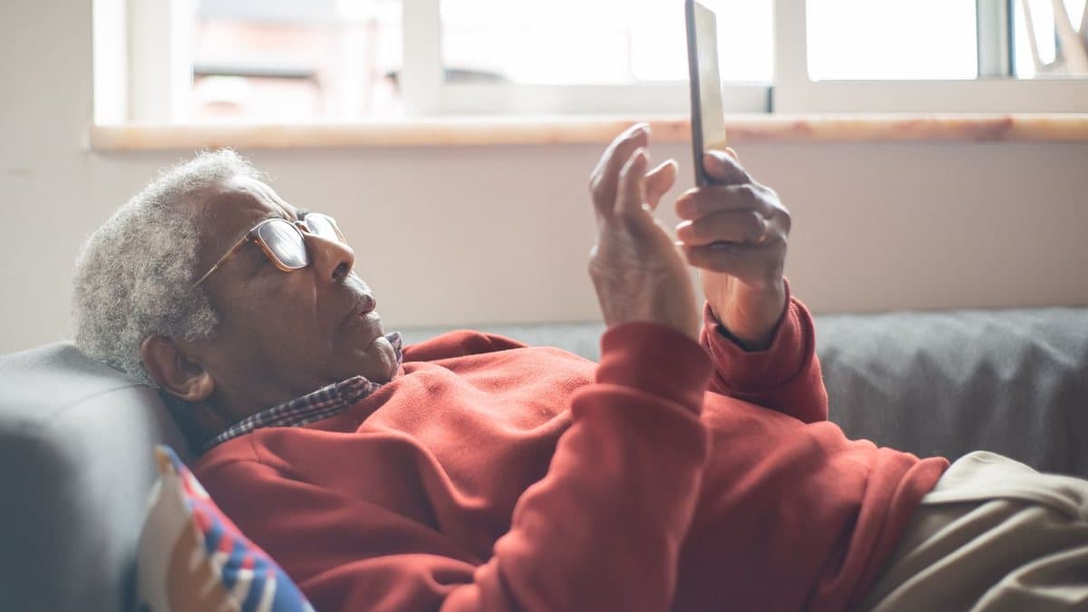 Person lying on a couch using a mobile device near the television
